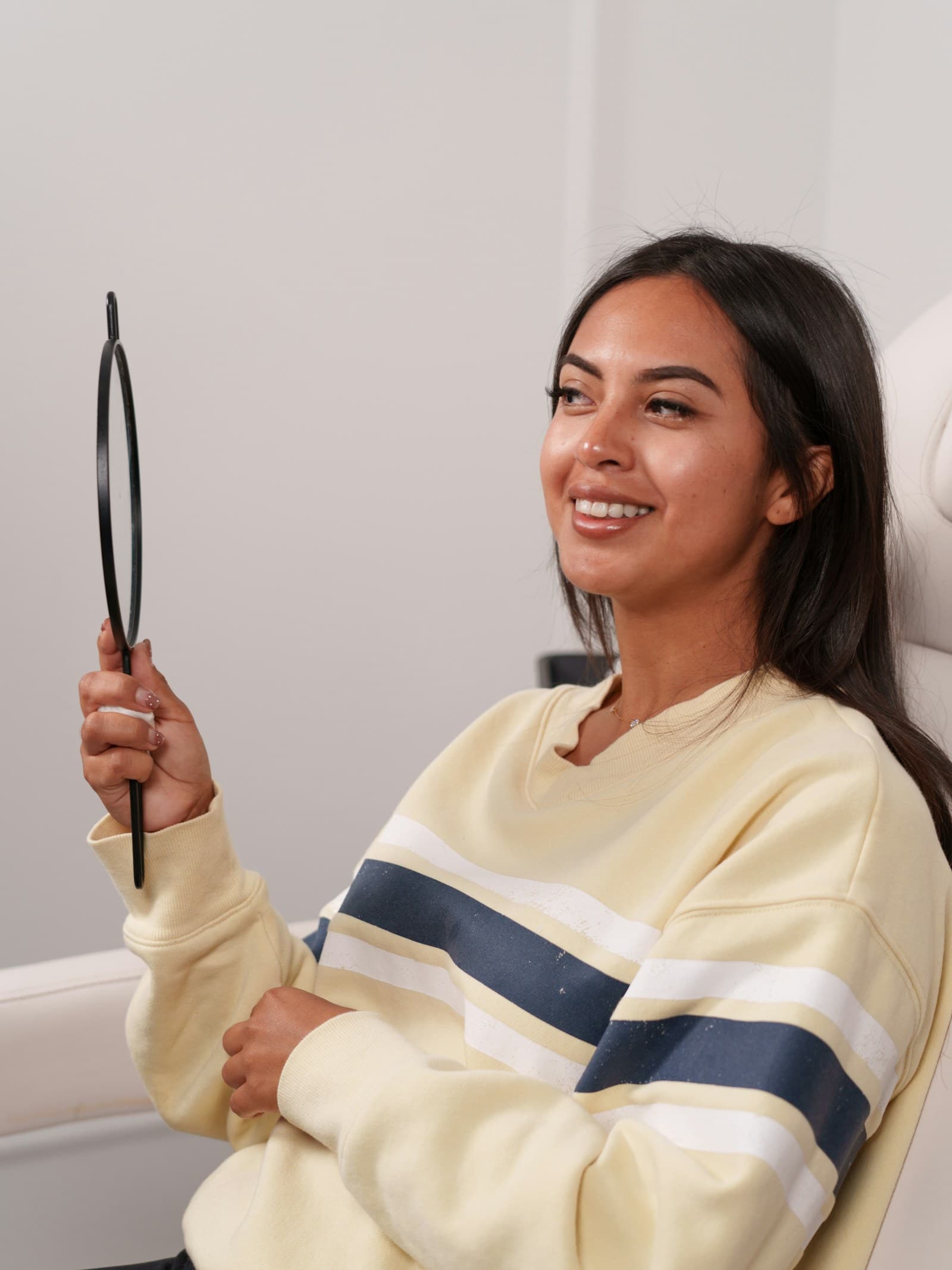 A smiling patient looking at their smile in a hand mirror